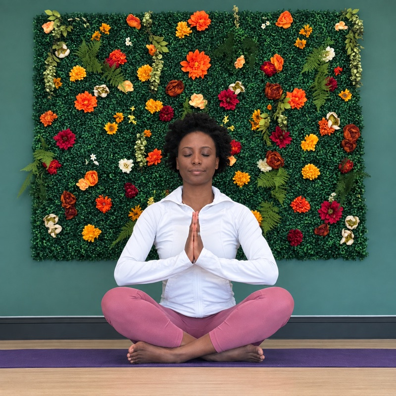 Wendy Bien-Aime seated in a meditative pose in front of a floral wall
